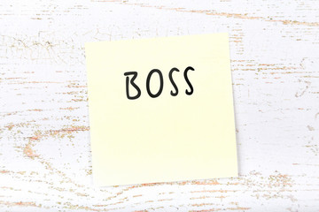 Yellow sticky note on wooden desk with handwritten text boss