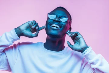 Keuken spatwand met foto Young african man listening to music with earphones, dancing isolated on pink background © Damir Khabirov