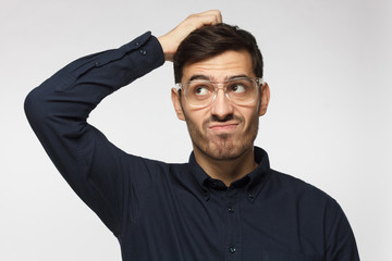 Caucasian man wearing glasses isolated on grey background scratching his head trying to find...