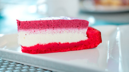 Piece of red berry mousse cake on a white plate in cafe. Sweet dessert concept.