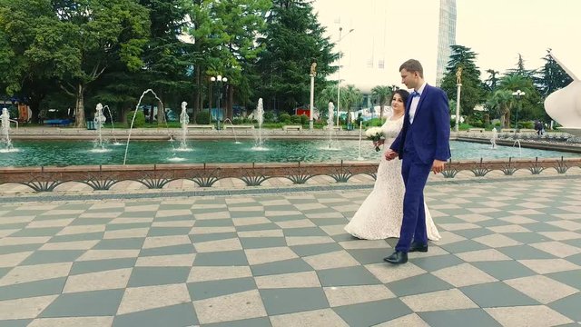 Bride and groom walk along the promenade along the fountains in Batumi