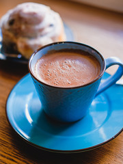 Brown cacao in bright blue mug and cinnamon bun on a wooden table.