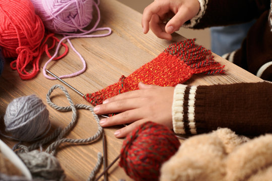 Child boy is learning to knit. Colorful wool yarns are on the wooden table. Hand closeup.