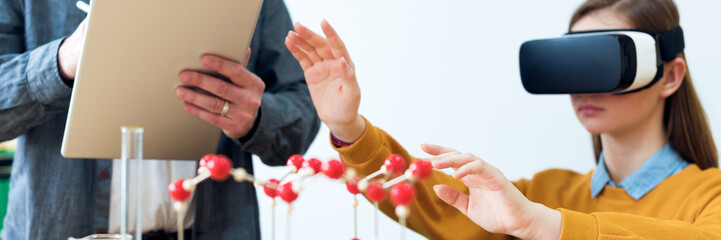 Young teacher using Virtual Reality Glasses and 3D presentation to teach students in chemistry class. Education, VR, Tutoring, New Technologies and Teaching Methods concept.