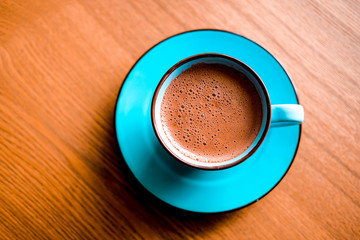 Brown cacao in bright blue mug on a wooden table.