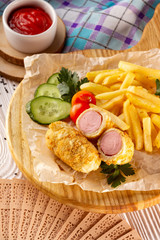 Vertical image of french hot dog with vegetables, fried potato and ketchup on wooden tray at decorated table background.