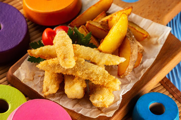 Closeup image of crispy golden nuggets and french fries at wooden tray board at decorated with colorful toys background.