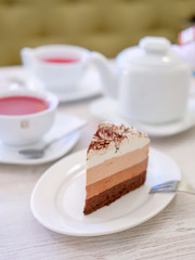 Piece of triple chocolate mousse cake on a white plate in cafe. Sweet dessert concept.