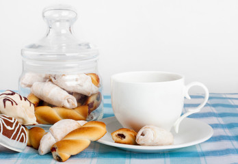 Cup of hot tea with fresh cookies and candy on checkered tablecloth
