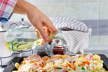 Man pouring olive oil raw chicken with vegetables