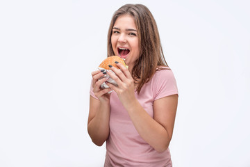 Happy young woman look on camera with mouth opened. She hold burger with both hands. Isolated on white background.