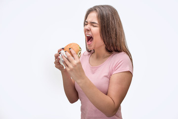 Young women keep mouth opened. She hold burger in hands. Model is going to eat it. Isolated on grey background.
