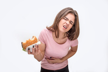 Young woman suffer from pain in stomach. She hold bitten burger. Another hand is on stomach area....