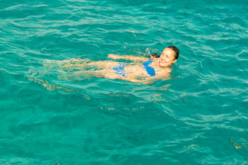 Young woman smiles, swiming in ocean. Young woman in bikini swimming in clear water.