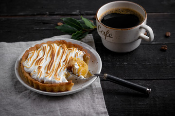 Hand made tart, tartlet with lemon curd and meringue and cup of coffee on a black wooden background. Selective focus, top view