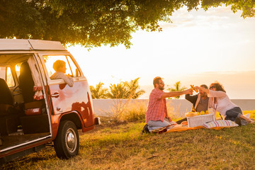 Family and friends all together in picnic leisure activity on a meadow with a red old vintage van...
