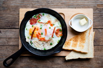 This delicious dish are eggs and sausage are fried cook in black small pan and put vegetables on top then serve with toast bread and butter for serving as breakfast, lunch or dinner.