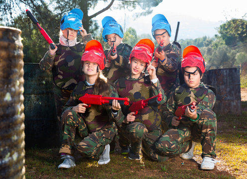 Friendly group of children paintball players in camouflage posing with guns on paintball playing field outdoors