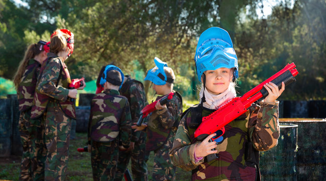 Teen girl wearing uniform and holding gun ready for playing with friends on paintball outdoor