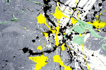 a spot of white and black and yellow and green spilled paint on a concrete textured surface