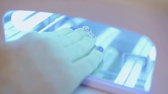 Woman dries her nails with shellac in UV lamp. Close-up.