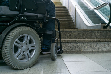 Closeup photo of man on a wheelchair in front of escalators and staircase with copy space