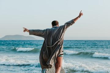 Young man in a bathrobe on the beach in sunset