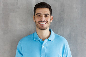 Portrait of smiling handsome man in blue polo shirt isolated on gray textured wall