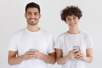 Young couple holding mobile phones, standing together and looking at camera, isolated on gray background