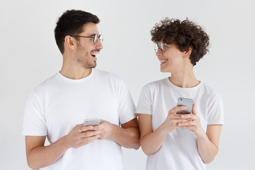 Young couple shocked with new app on their phones, looking at each other, isolated on gray background