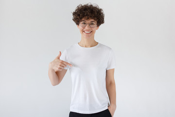 Daylight shot of smiling woman pointing at  blank white t-shirt with index finger, copy space for...