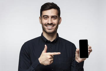 Young man holding smartphone in hand and pointing to it with finger