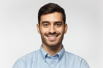 Closeup headshot of businessman standing against gray background, smiling with satisfaction and confidence