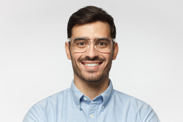 Smart businessman smiling at camera, wearing trendy transparent glasses, isolated on gray background