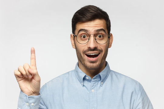 Studio shot of university teacher raises index finger, having a good idea, isolated on gray background