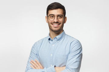 Handsome smiling business man in blue shirt standing with crossed arms, isolated on gray background