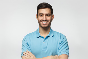 Portrait of smiling handsome man in blue polo shirt, standing with crossed arms isolated on grey background