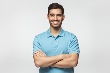 Smiling handsome man in blue polo shirt standing with crossed arms isolated on gray background - Powered by Adobe