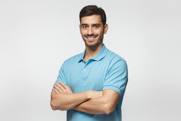 Portrait of attractive young sporty man in blue polo shirt standing with crossed arms, isolated on...