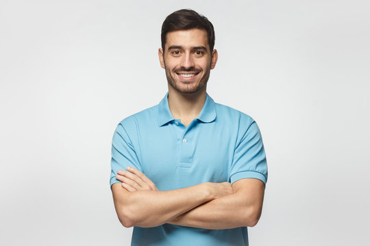 Smiling handsome man in blue polo shirt standing with crossed arms isolated on gray background