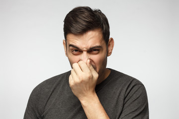 Close-up portrait of young man holding his nose as if smelling something rotten and stinky, trying to find source of odor