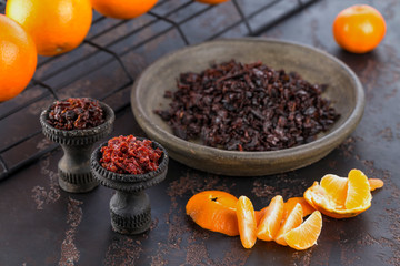 Two black burnt ceramic bowls for hookah Smoking are filled with different types of hookah on the background of ripe oranges and tangerines