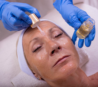 Close up of beautiful senior woman during facial skin treatment with face serum 