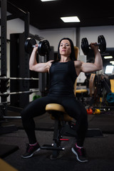 Fototapeta na wymiar fitness girl trains with dumbbells in the gym. Pumps the deltoid muscles