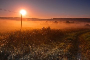 The hot morning sun rises above the rural landscape and road