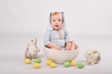 Toddler boy in an Easter bunny costume on a light background with Easter eggs