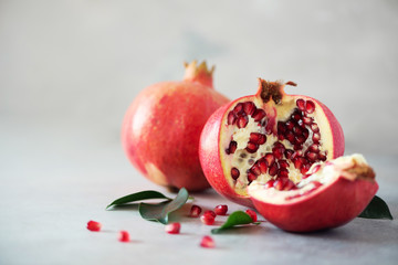 Ripe pomegranate fruit with green leaves on grey concrete background. Banner with copy space