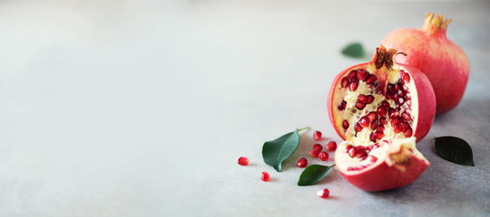 Ripe pomegranate fruit with green leaves on grey concrete background. Banner with copy space. Vegan, healthy diet concept
