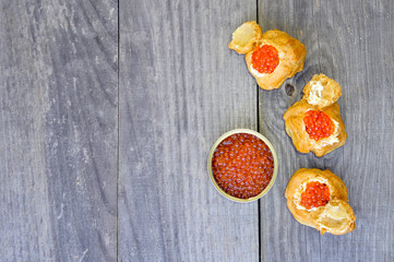 Eclairs with red caviar on wooden rustic vintage background.