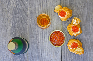 Eclairs with red caviar, caviar in a tin, a bottle and a glass of cognac on a wooden rustic vintage background.